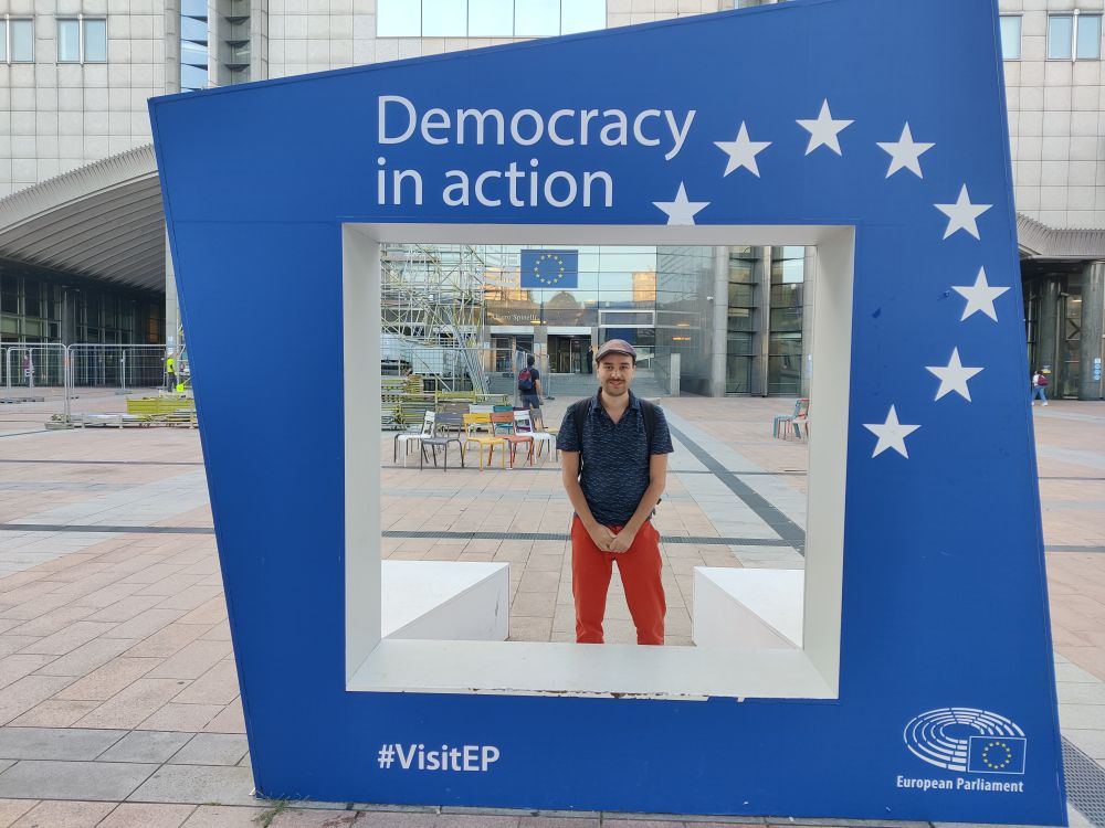 Picture of Carl Schwan in front of the European Parlament and a sign “Democraty in Action”